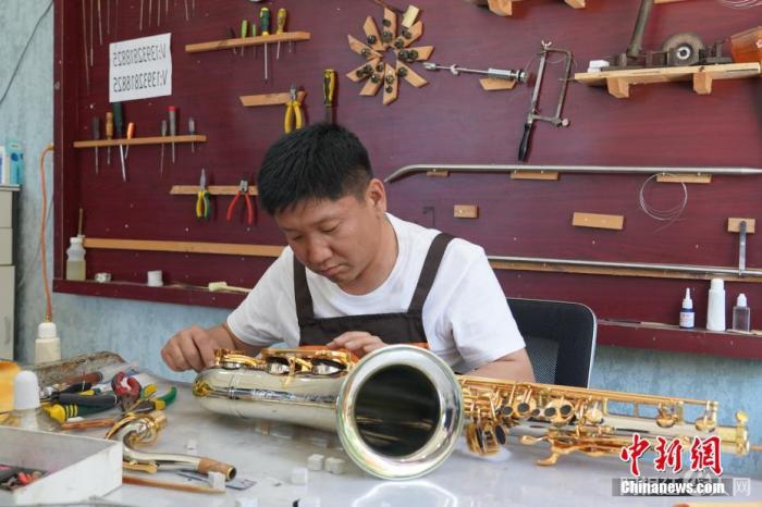 图为5月26日,周窝村村民周卫仓维修萨克斯。周卫仓在音乐小镇建设之初回到家乡创业,建起“小周工作室”。 中新社发 徐鹏璐 摄 图为5月26日,周窝村村民周卫仓维修萨克斯。周卫仓在音乐小镇建设之初回到家乡创业,建起“小周工作室”。 中新社发 徐鹏璐 摄