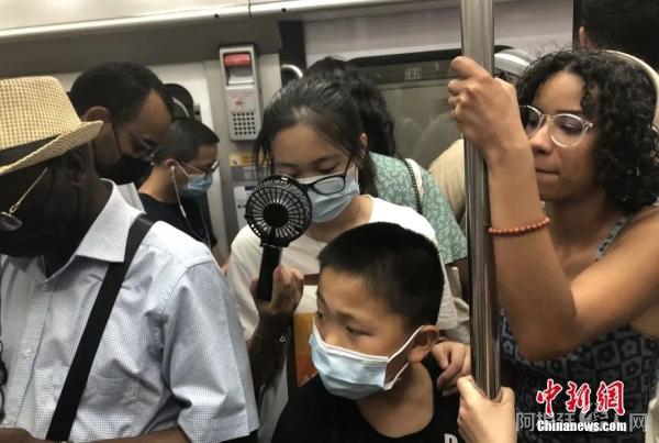 当地时间7月19日，法国首都巴黎气温突破40摄氏度。当天仍有不少民众选择乘坐地铁出行。图为在拥挤的巴黎地铁车厢内，有民众用微型风扇解暑。中新社记者 李洋 摄
